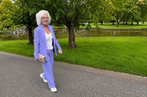 Netty 91 Netty loopt lachend in een lila broekpak door een groen park.